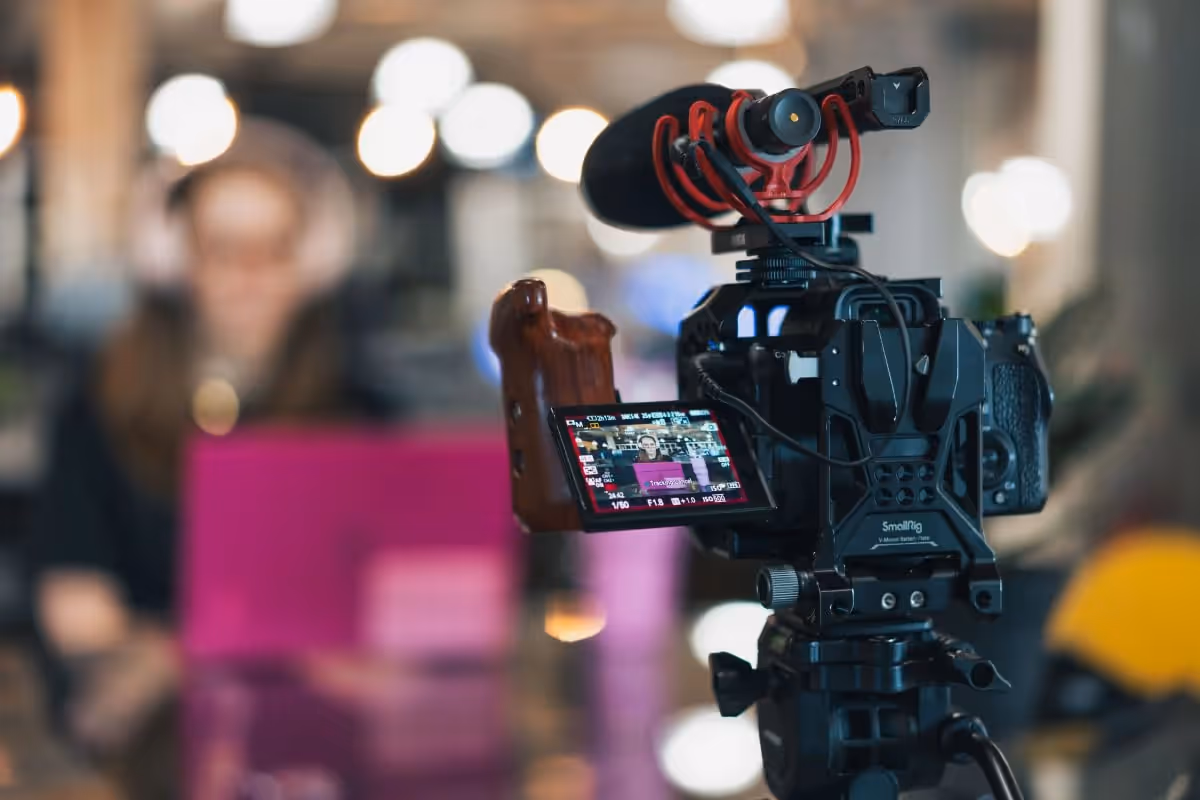 A cinema camera and shotgun mic on a tripod film an interview in a softly lit office.