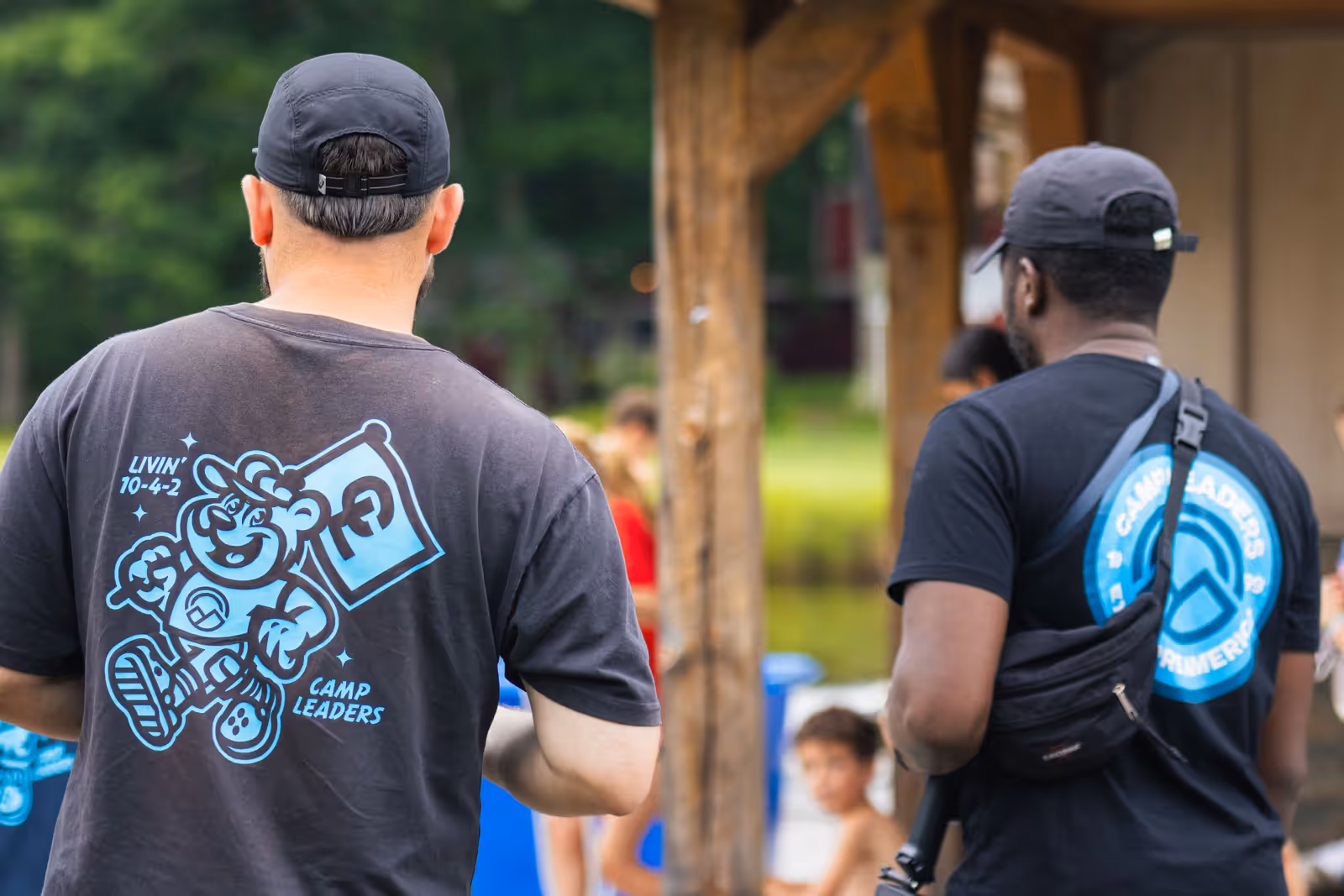 Two crew members in Camp Leaders t-shirts watch the afternoon's filming from beside the pool shelter.