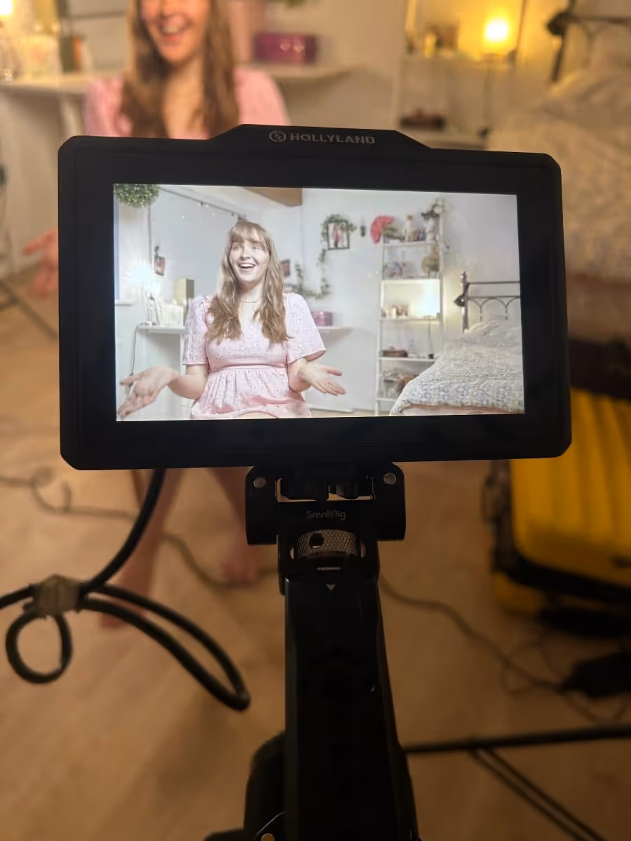 A director's field monitor shows an interview being filmed on a bedroom set.